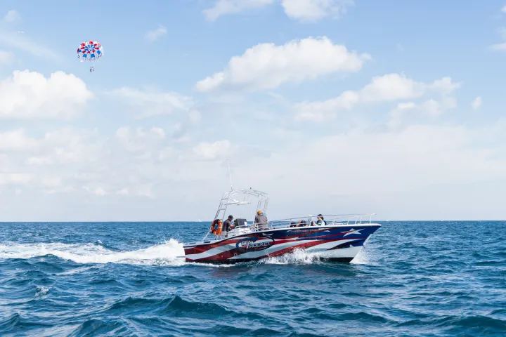 Boat with American flag design on ocean, parasail in sky.