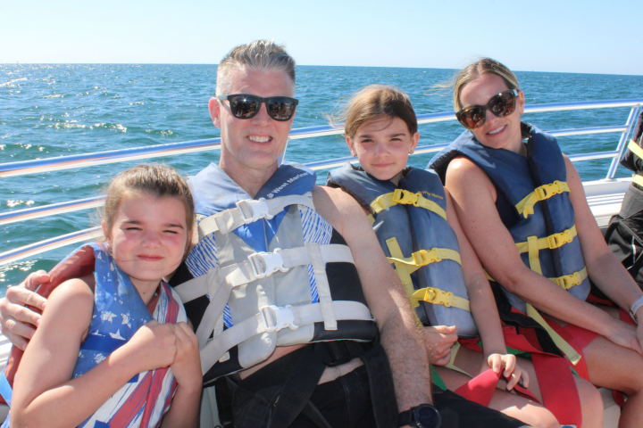 Family wearing life vests on a boat with ocean view.