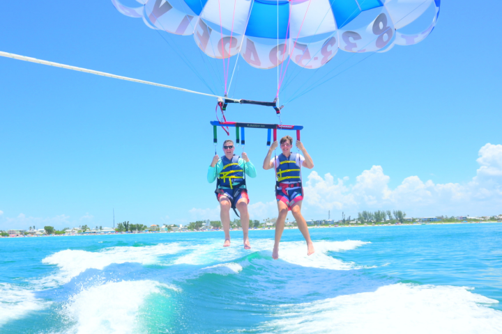 Two people parasailing over the ocean with colorful parachute against a clear blue sky.