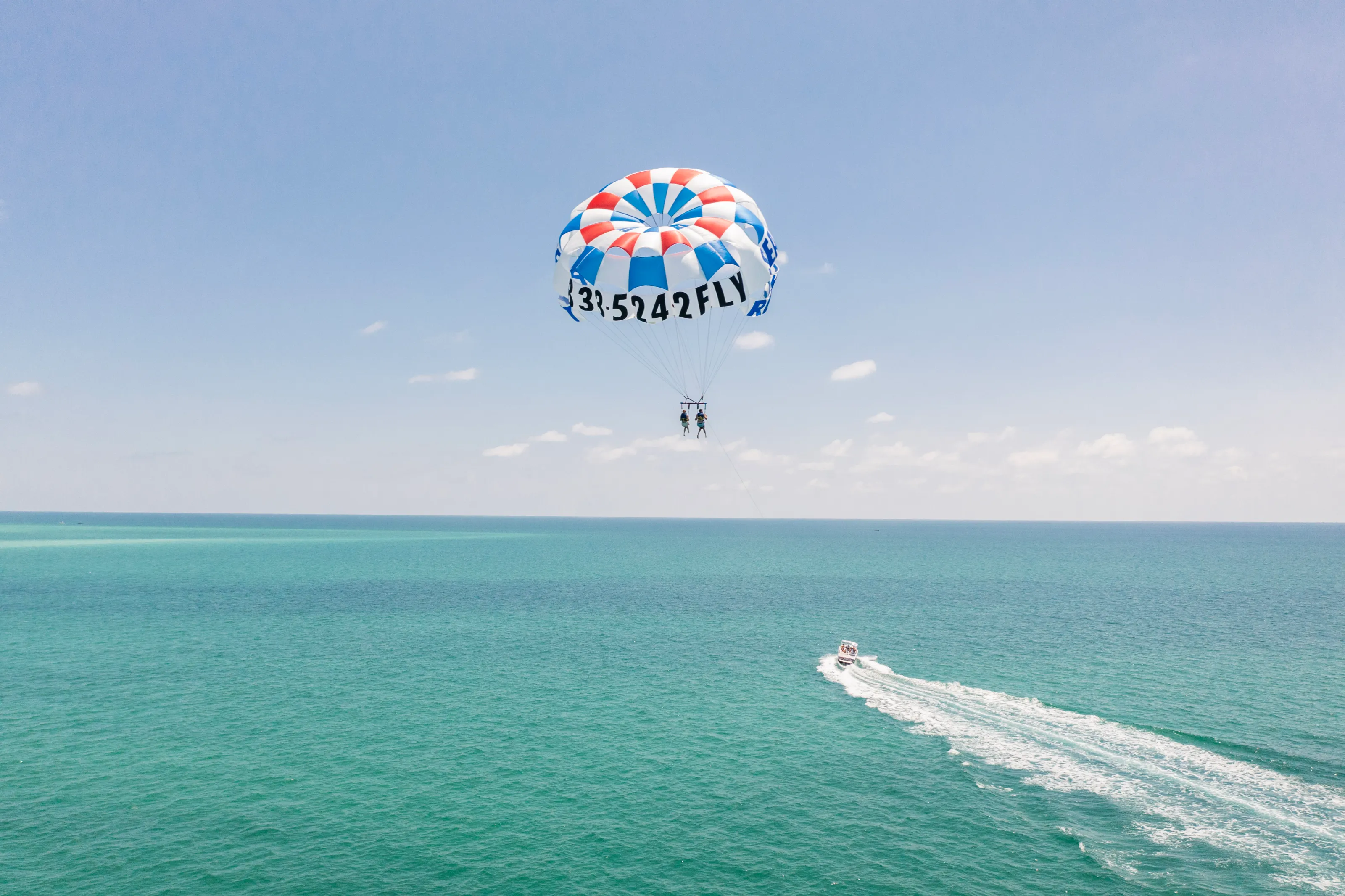 Parasailing over the ocean with a colorful parachute and a boat towing.