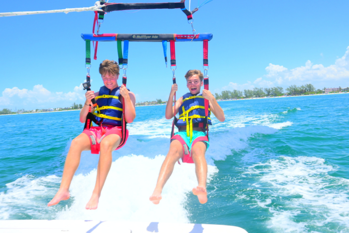 Two people parasailing over the ocean with clear skies and distant shoreline.