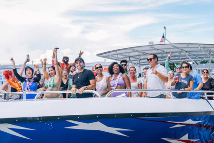 Group of people cheering on a boat with festive attire and drinks in hand.