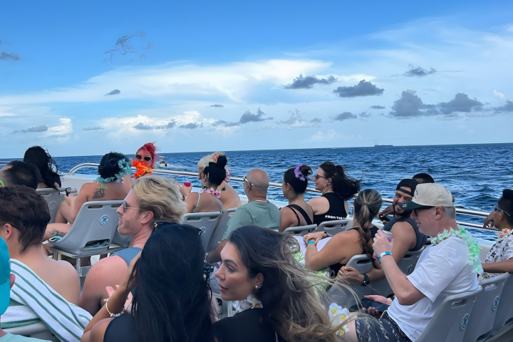 Group of people on a boat with blue ocean and cloudy sky in the background.