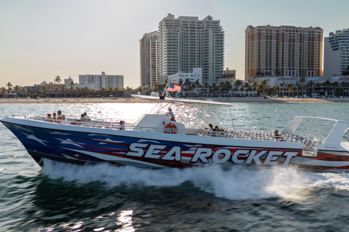 Speedboat named Sea Rocket on water, with buildings in the background and people onboard.