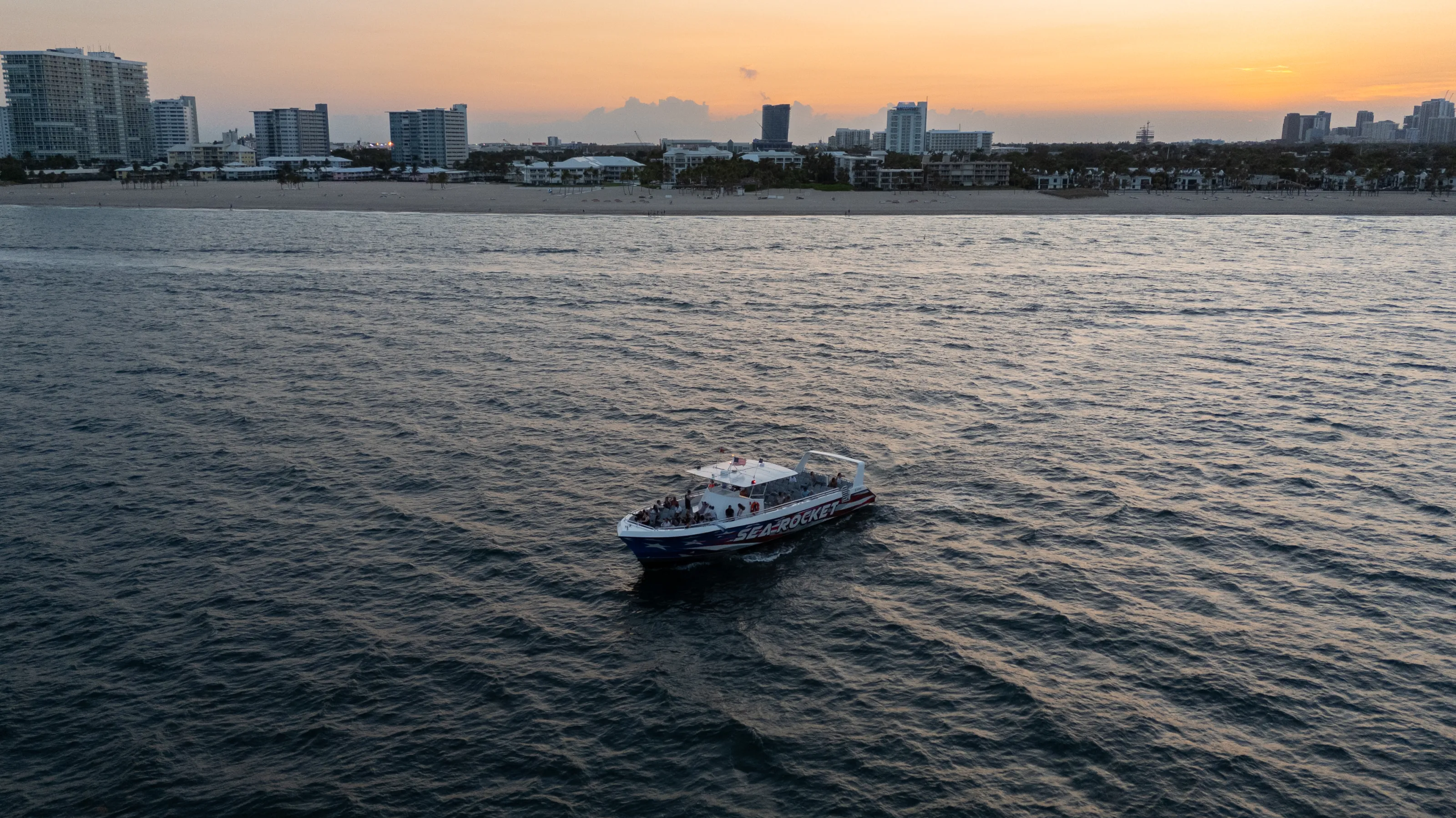 Boat on water with city skyline at sunset in the background.