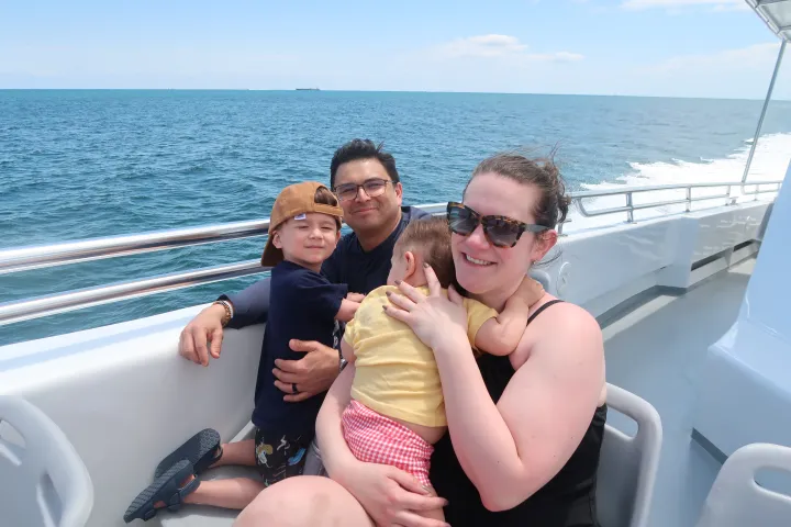 Family of four smiling on a boat with ocean in the background.