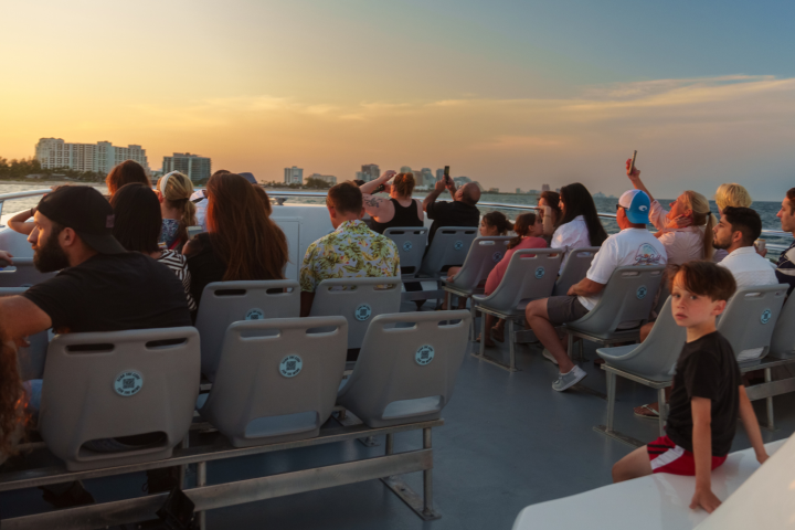 People on a boat watching sunset with city skyline in the background.