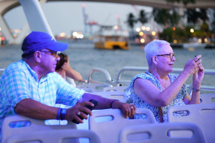 Two people on a boat at dusk, taking pictures with their phones.