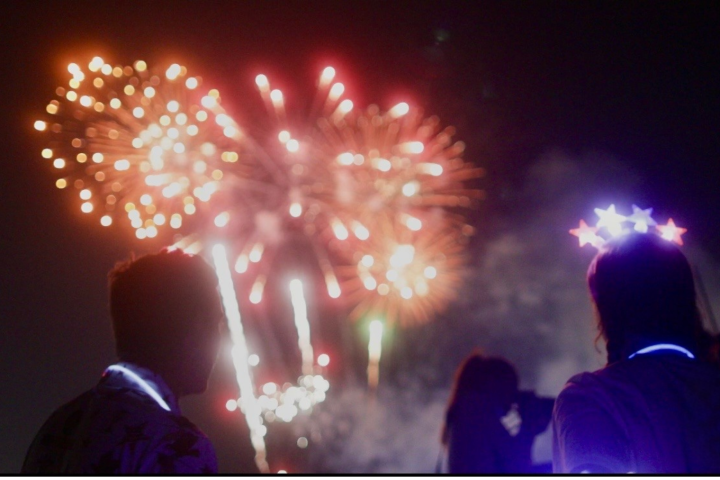Silhouetted people watching colorful fireworks in the night sky.