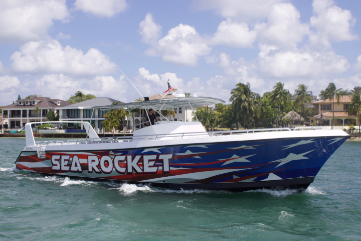 Speedboat 'Sea Rocket' with patriotic design on water, houses and palm trees in background.