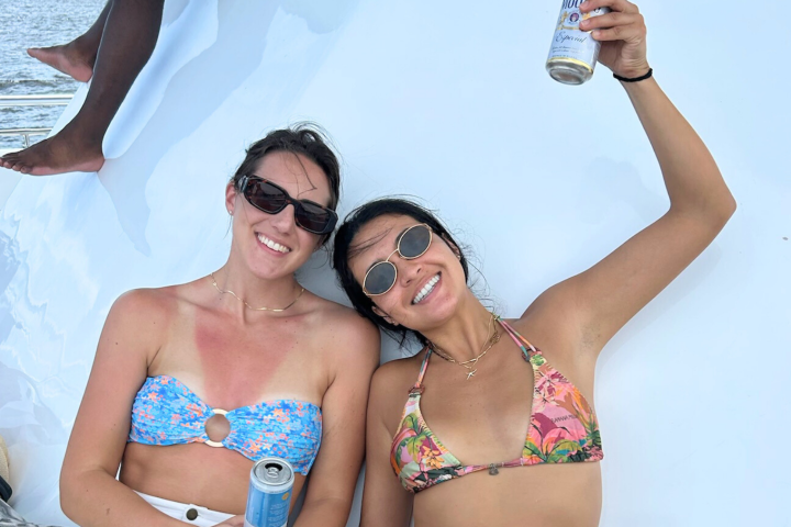 Two women in swimsuits relaxing on a boat, holding canned drinks.