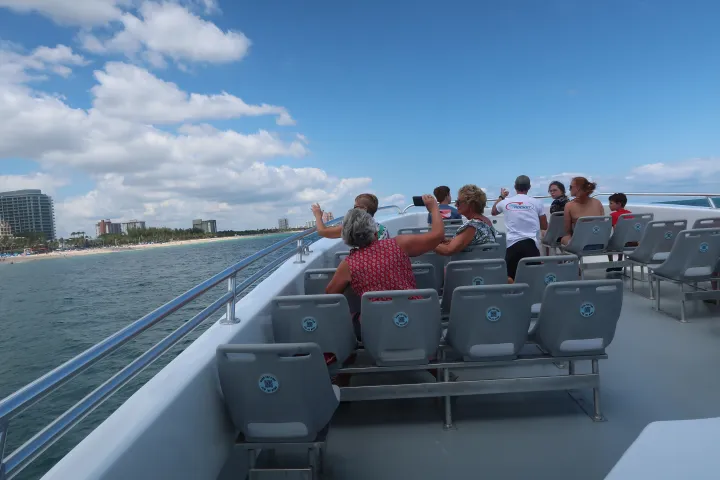 People seated on a boat deck enjoying a sunny cruise near the coastline.