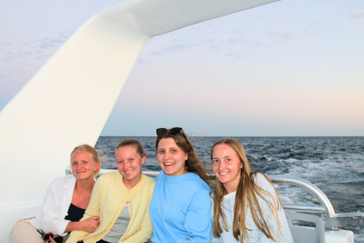 Four women sitting on a boat with ocean background.